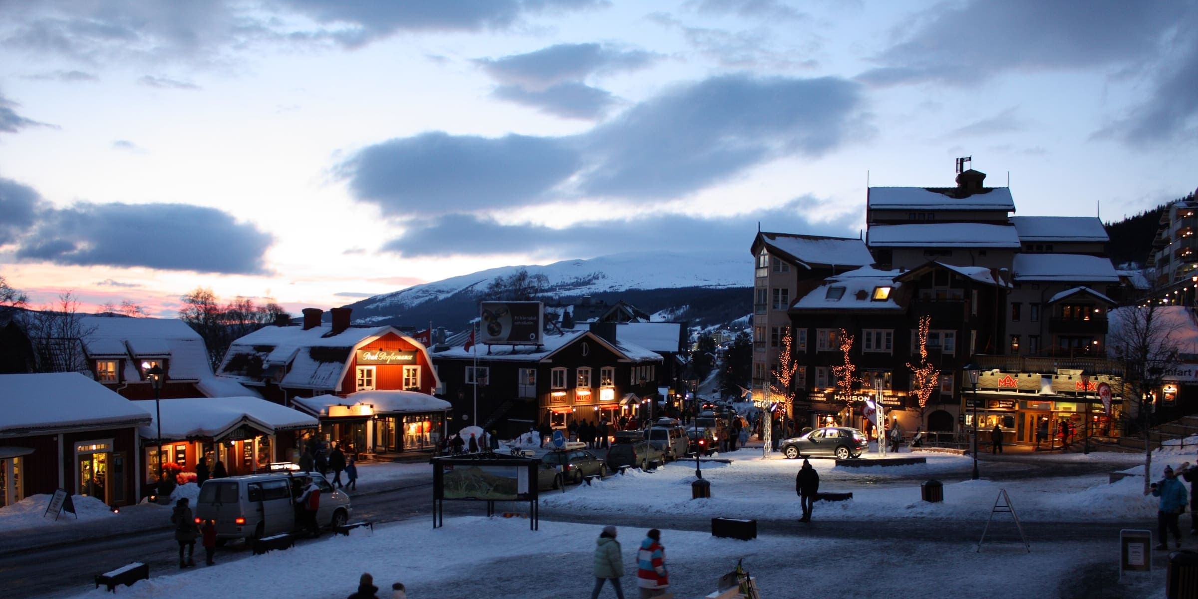 Åre's village square at dusk in winter, with the snowy slopes of Åreskutan behind