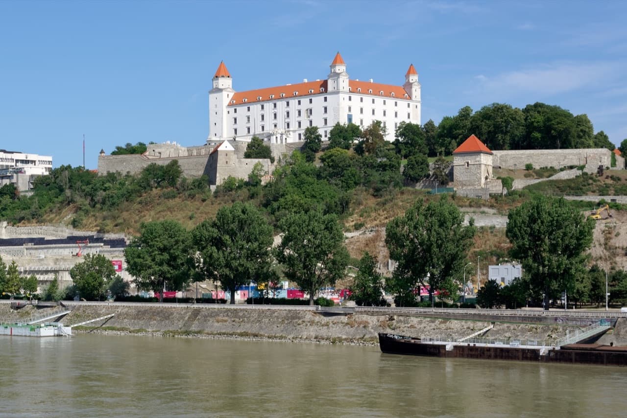 The white rectangular silhouette of Bratislava Castle standing high over the Danube River at sunset