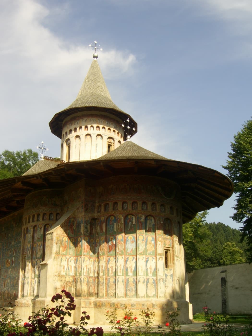 The brilliant blue external frescoes of Voroneț Monastery under wide eaves amidst rolling forested hills of Bucovina