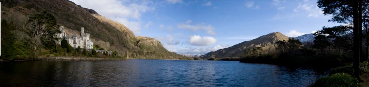 The Gothic castle towers of Kylemore Abbey mirrored in the waters of Pollacappall Lough beneath Connemara mountains