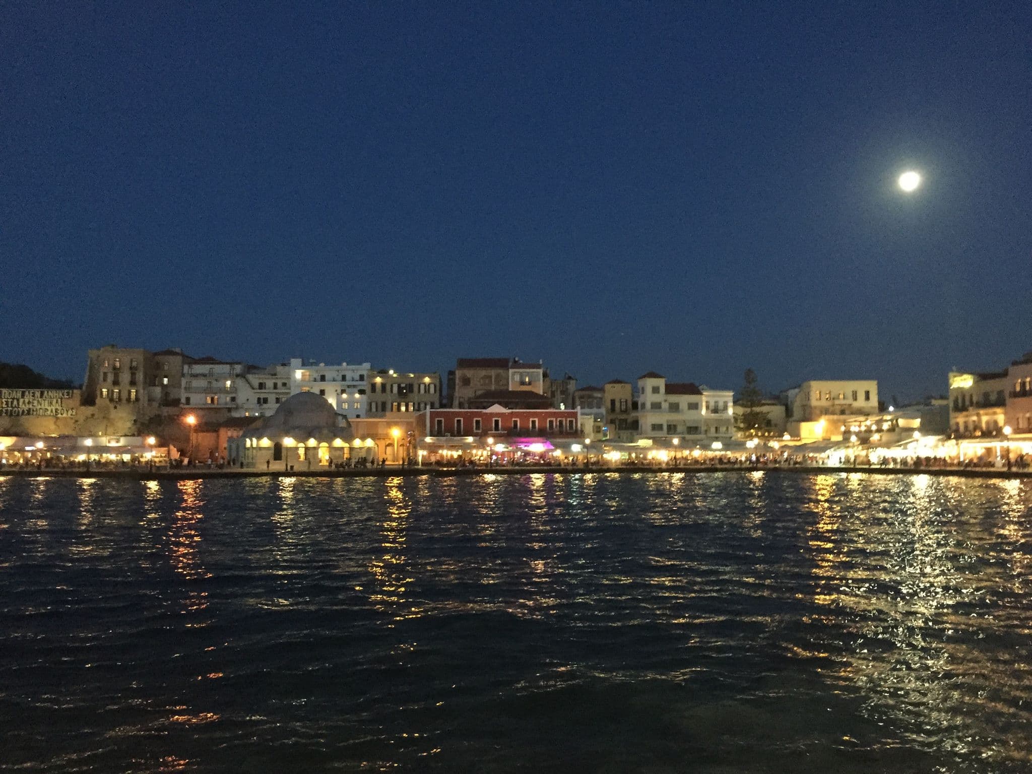 Venetian lighthouse and historic waterfront buildings reflected in the harbour at Chania, Crete
