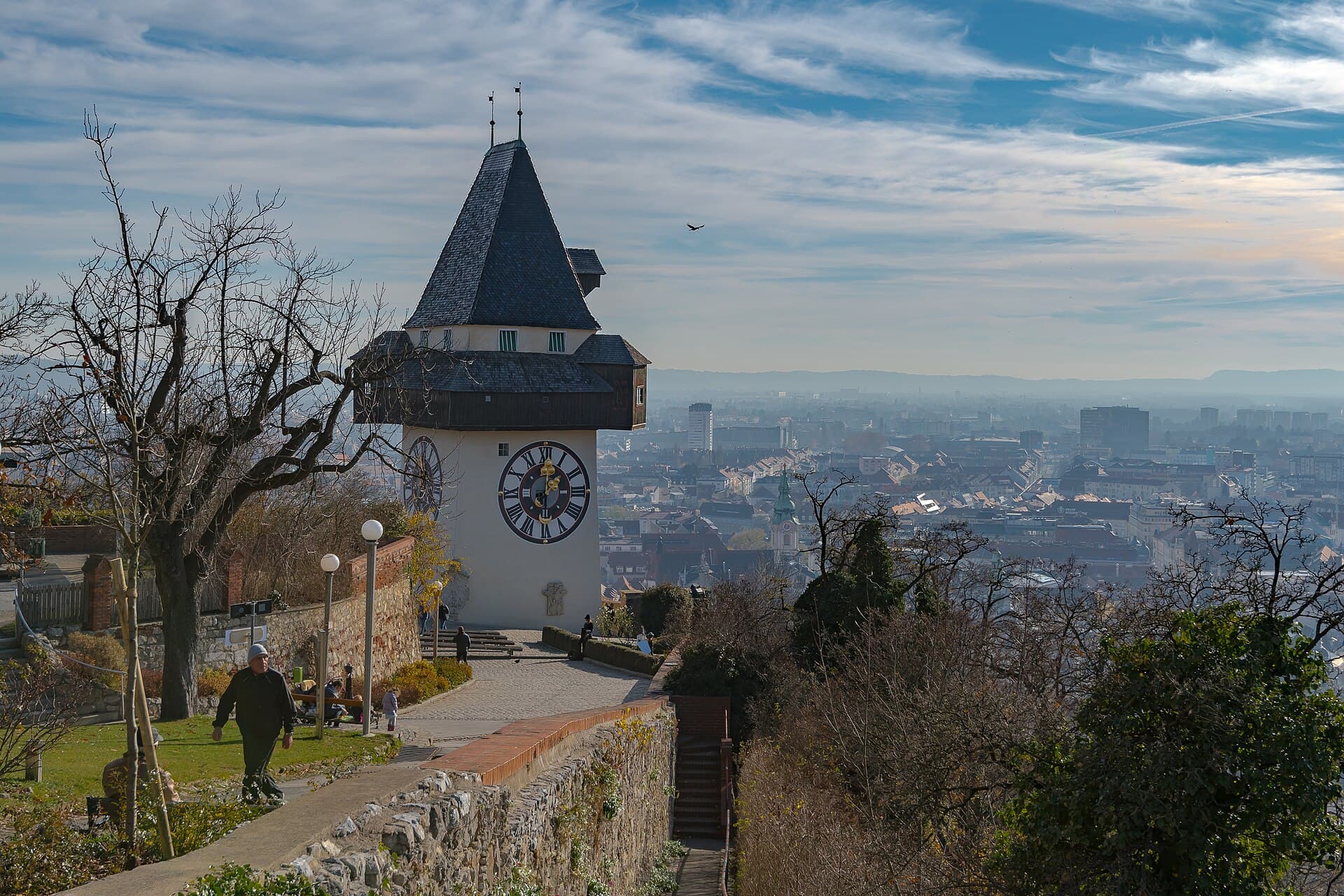 The historic Uhrturm clock tower crowning the forested Schlossberg hill above the terracotta rooftops of Graz