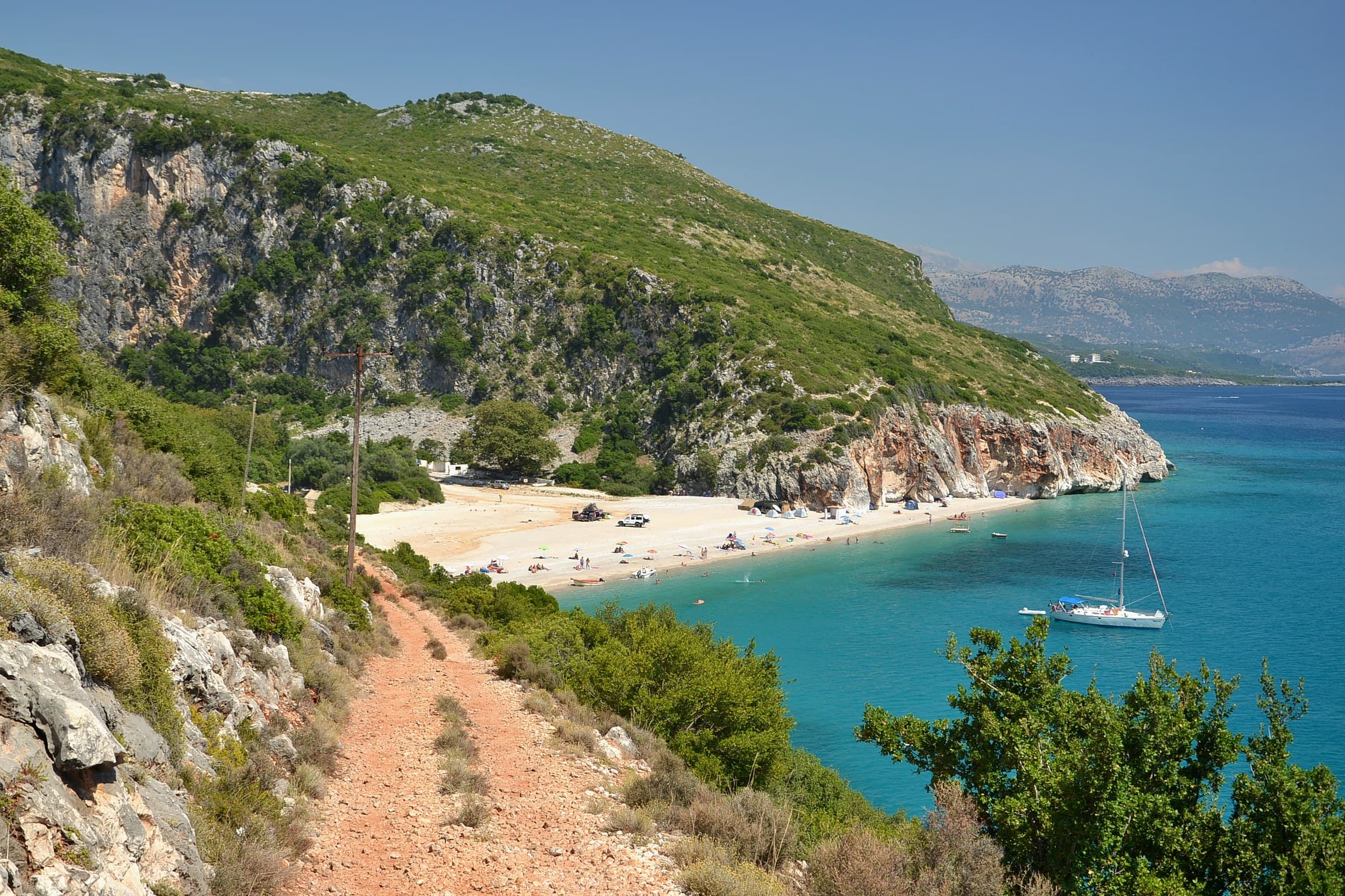 Pristine white pebble cove and turquoise waters of Gjipe Beach framed by sheer red canyon cliffs on the Riviera