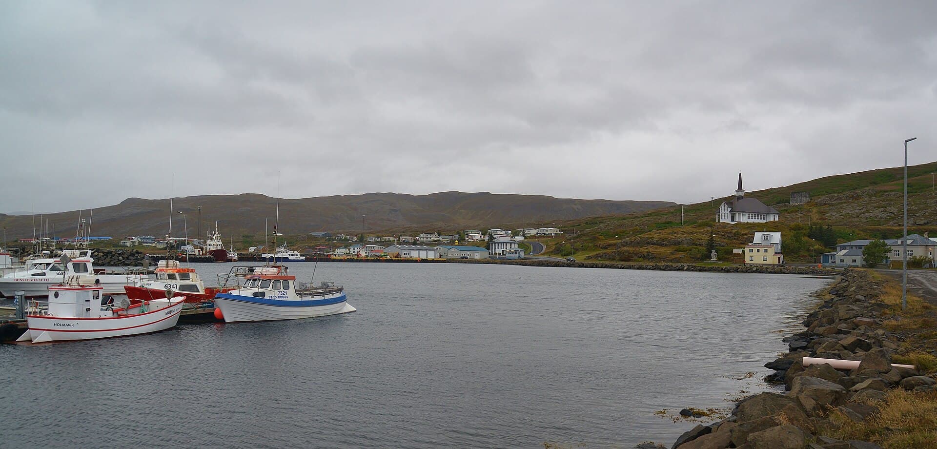 Sheltered coastal inlet and colorful wooden buildings of Hólmavík against the hills of Strandir