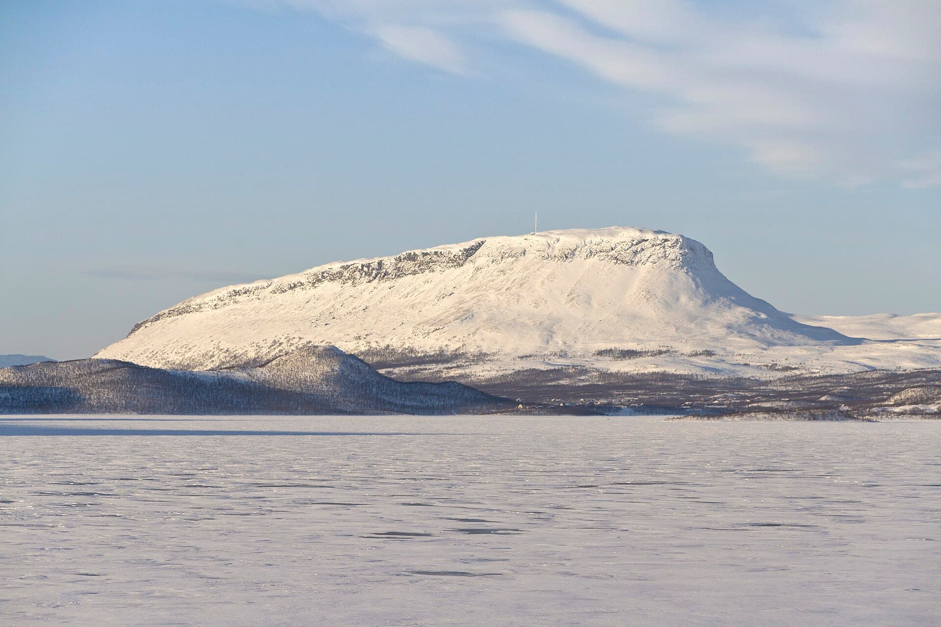 Iconic steep quartzite silhouette of sacred Mount Saana towering above the snowy expanse of Lake Kilpisjärvi in Lapland