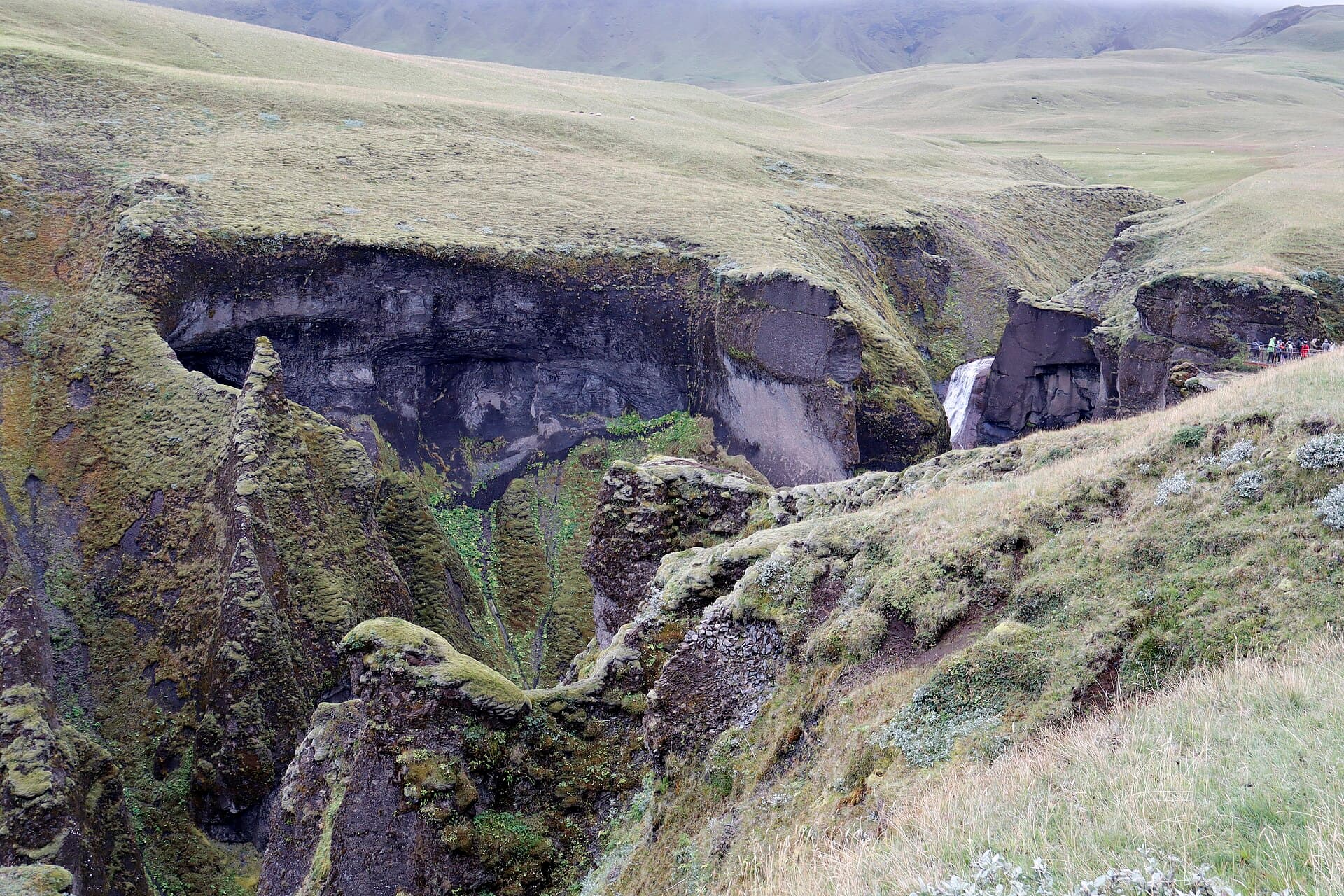 Winding turquoise glacial river flowing through the colossal green moss-covered canyon walls of Fjaðrárgljúfur
