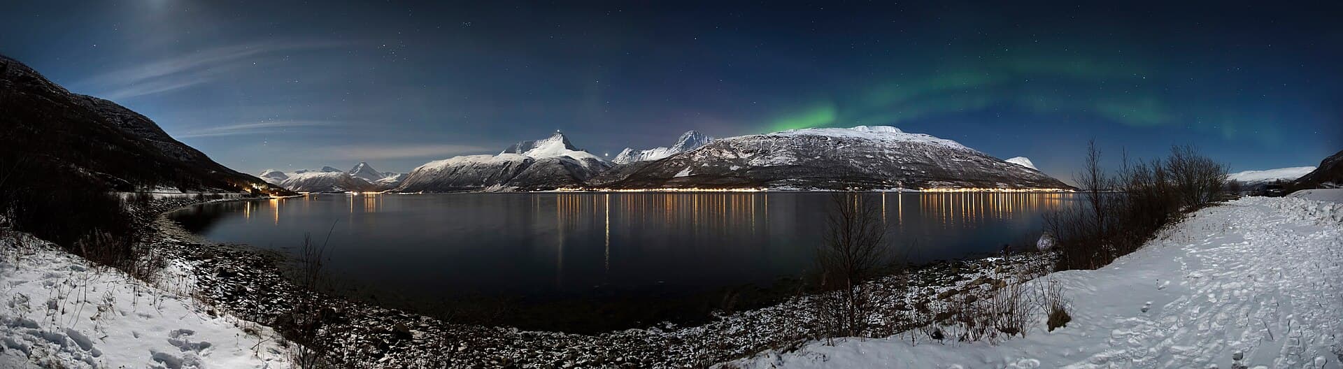 Jagged snow-capped peaks of the Lyngen Alps rising across the blue waters of Lyngenfjord in Troms.