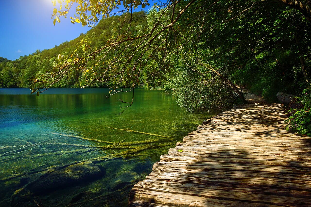 Curved wooden pedestrian boardwalk over emerald crystal waters in Plitvice Lakes National Park