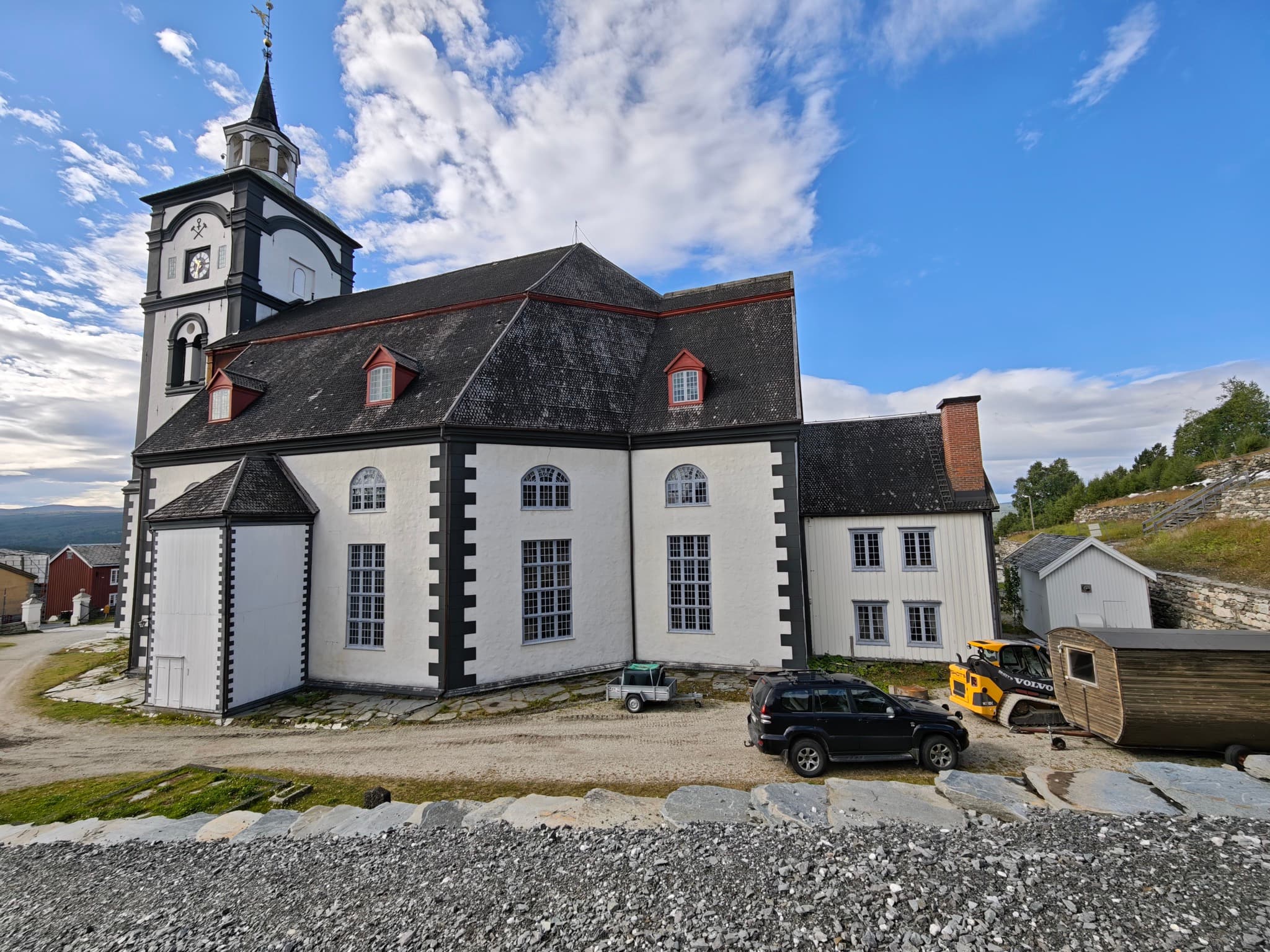 Snow-dusted dark timber historic houses and baroque stone church tower in the UNESCO mining town of Røros