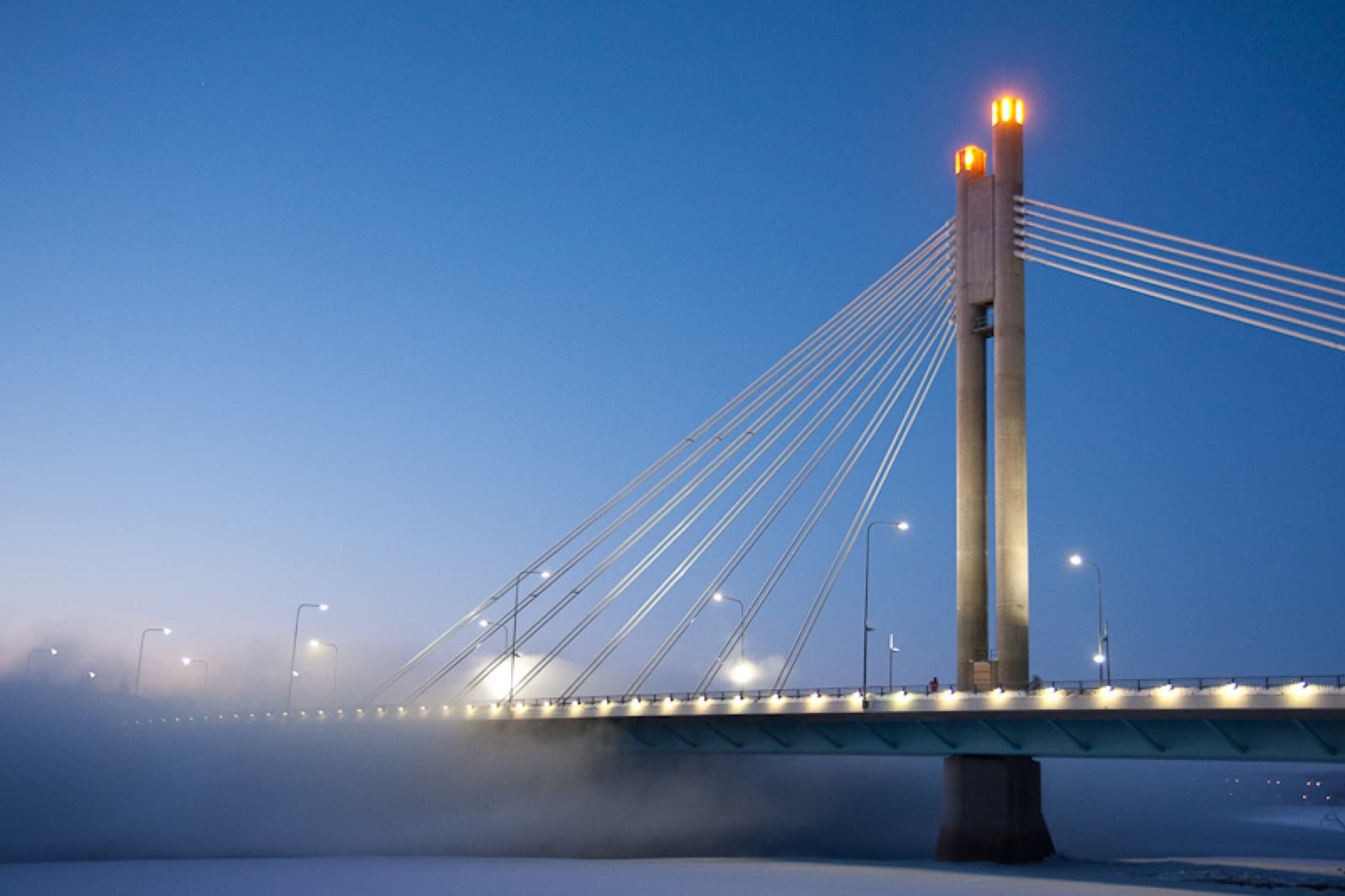 The illuminated glass crescent tunnel of the Arktikum Science Centre extending under snow towards the frozen Ounasjoki River in Rovaniemi