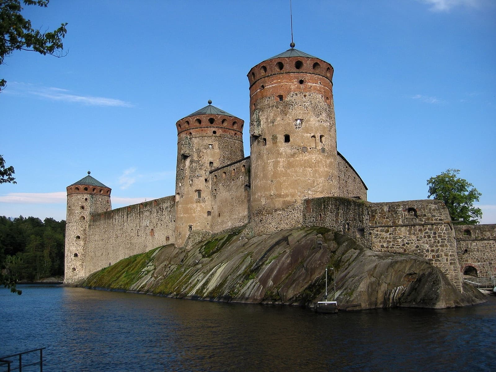 The imposing medieval cylindrical stone towers of Olavinlinna Castle perched on a rocky islet in the blue waters of Lake Saimaa