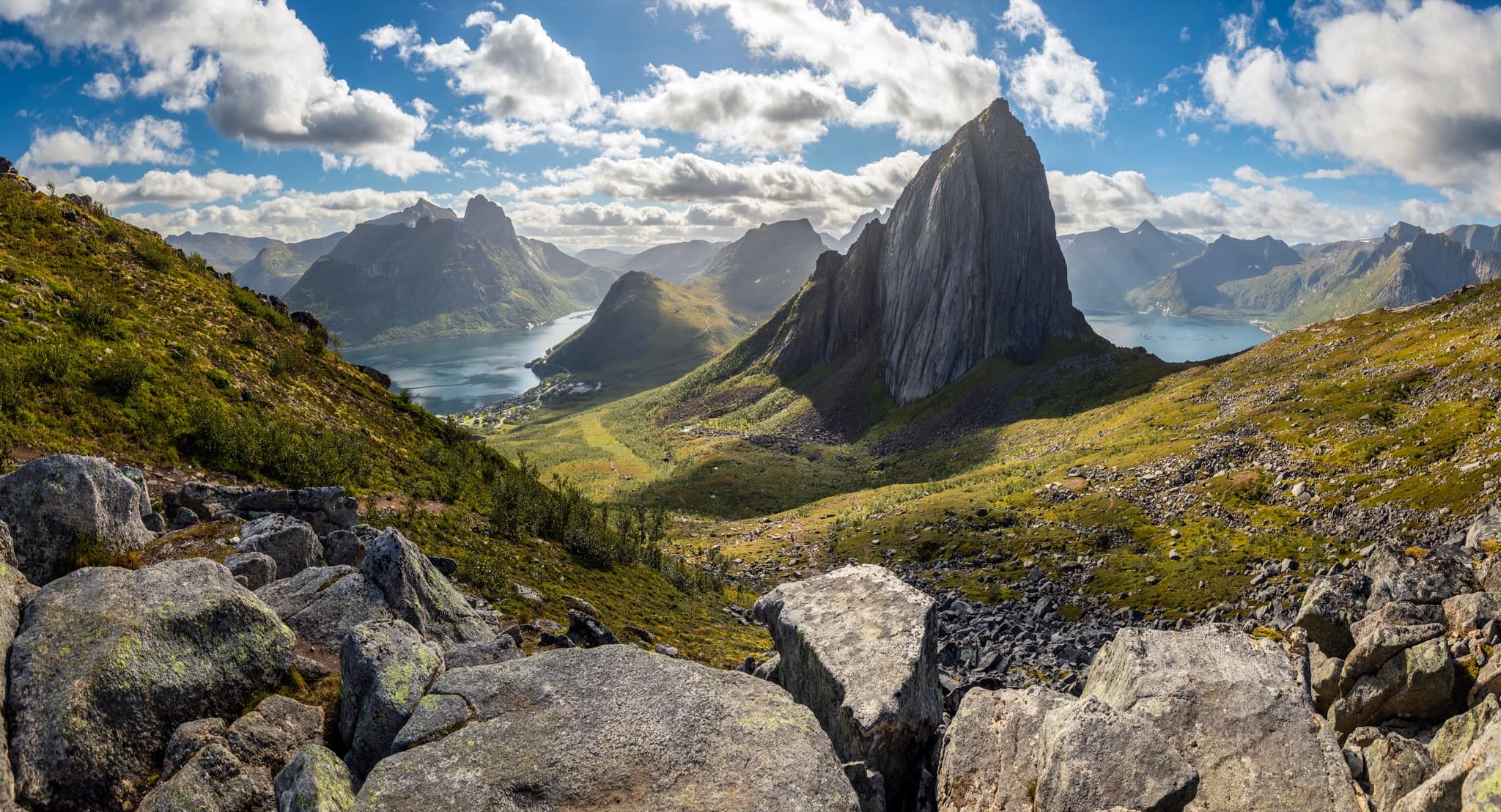 Sheer jagged granite peaks of Senja plunging dramatically into turquoise Arctic fjord waters under the midnight sun