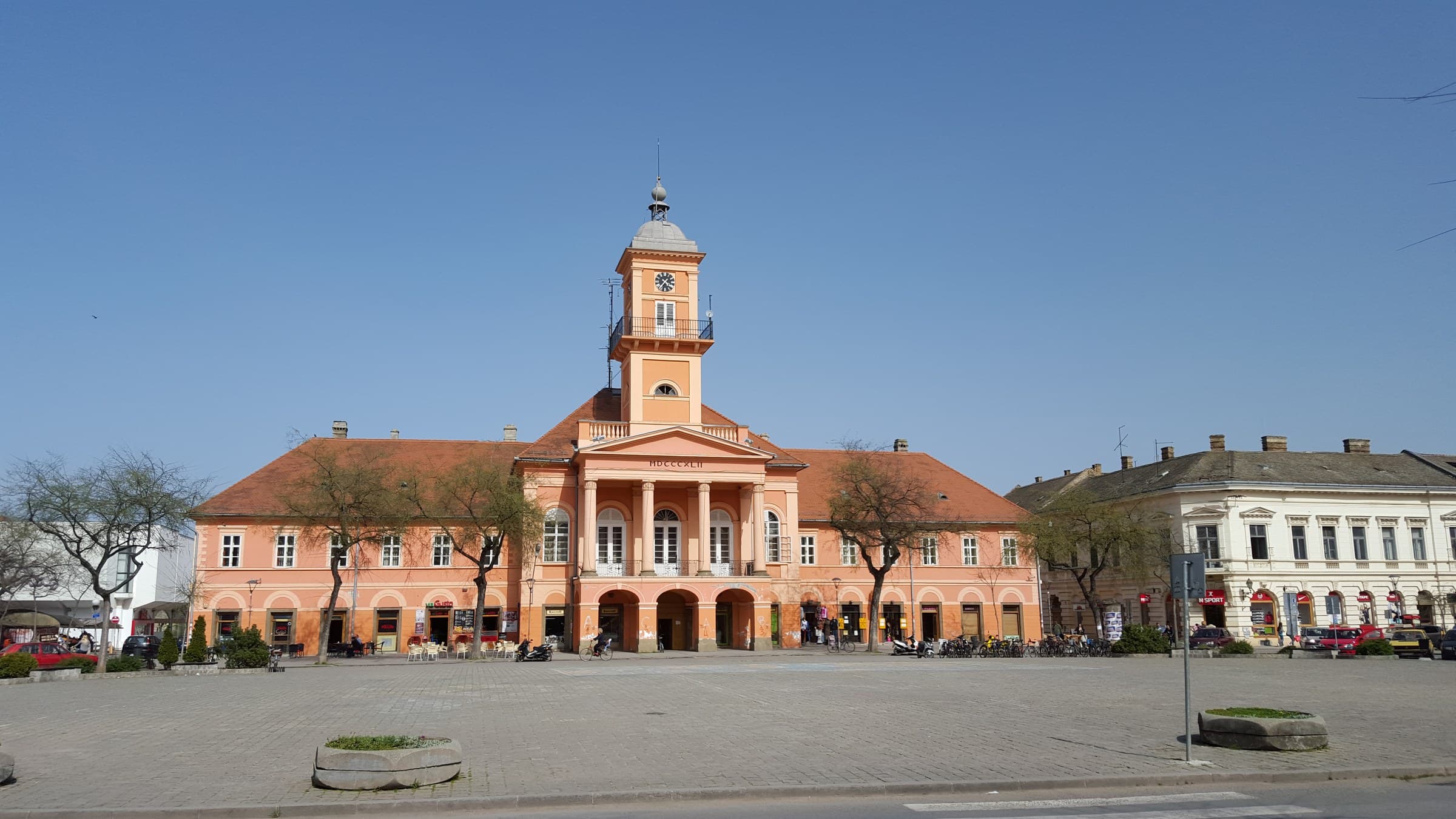 The ochre neoclassical County Hall of Sombor seen across its tree-shaded square