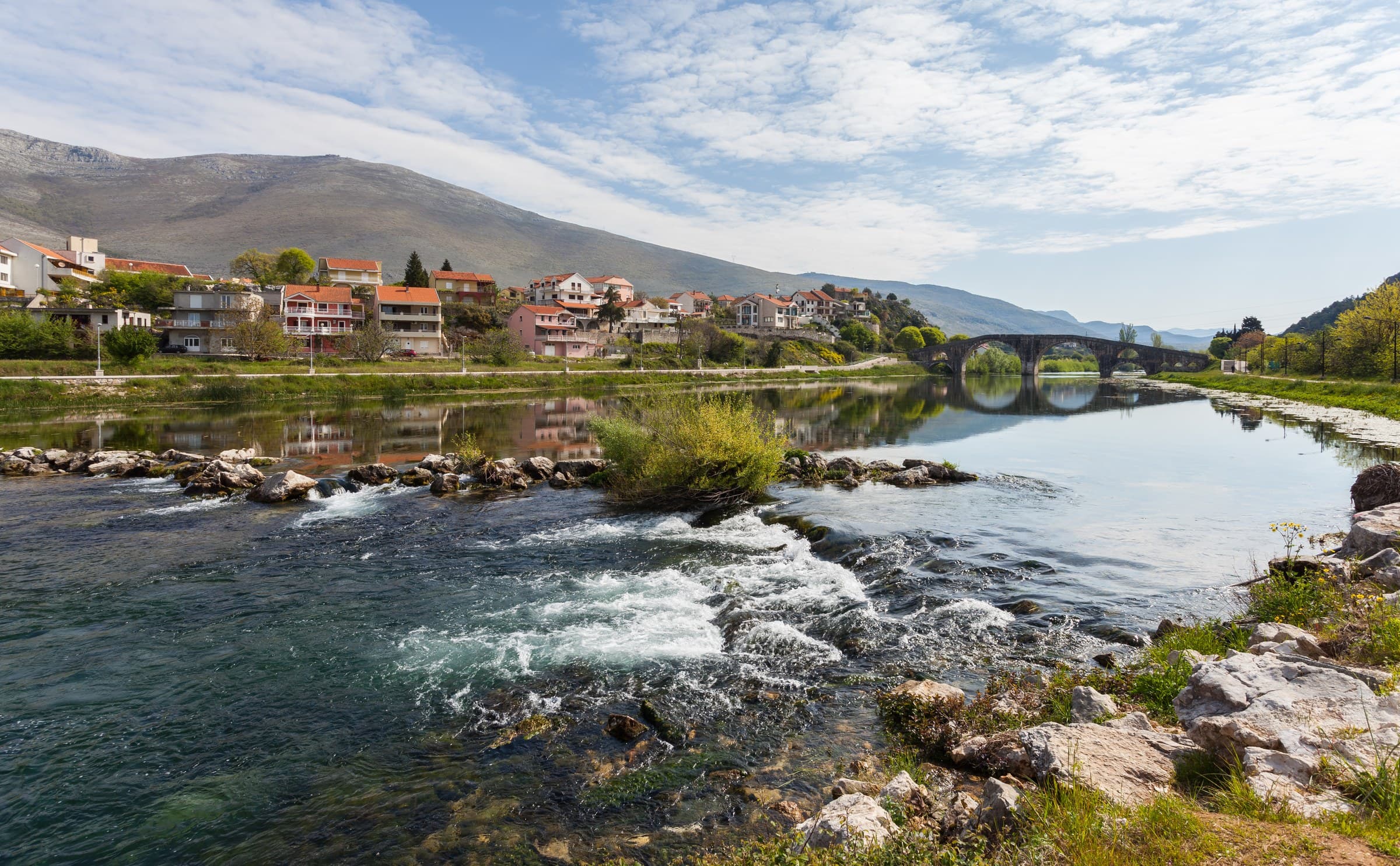 Arslanagić Bridge spanning the Trebišnjica River in sunny Mediterranean Trebinje framed by cypress trees