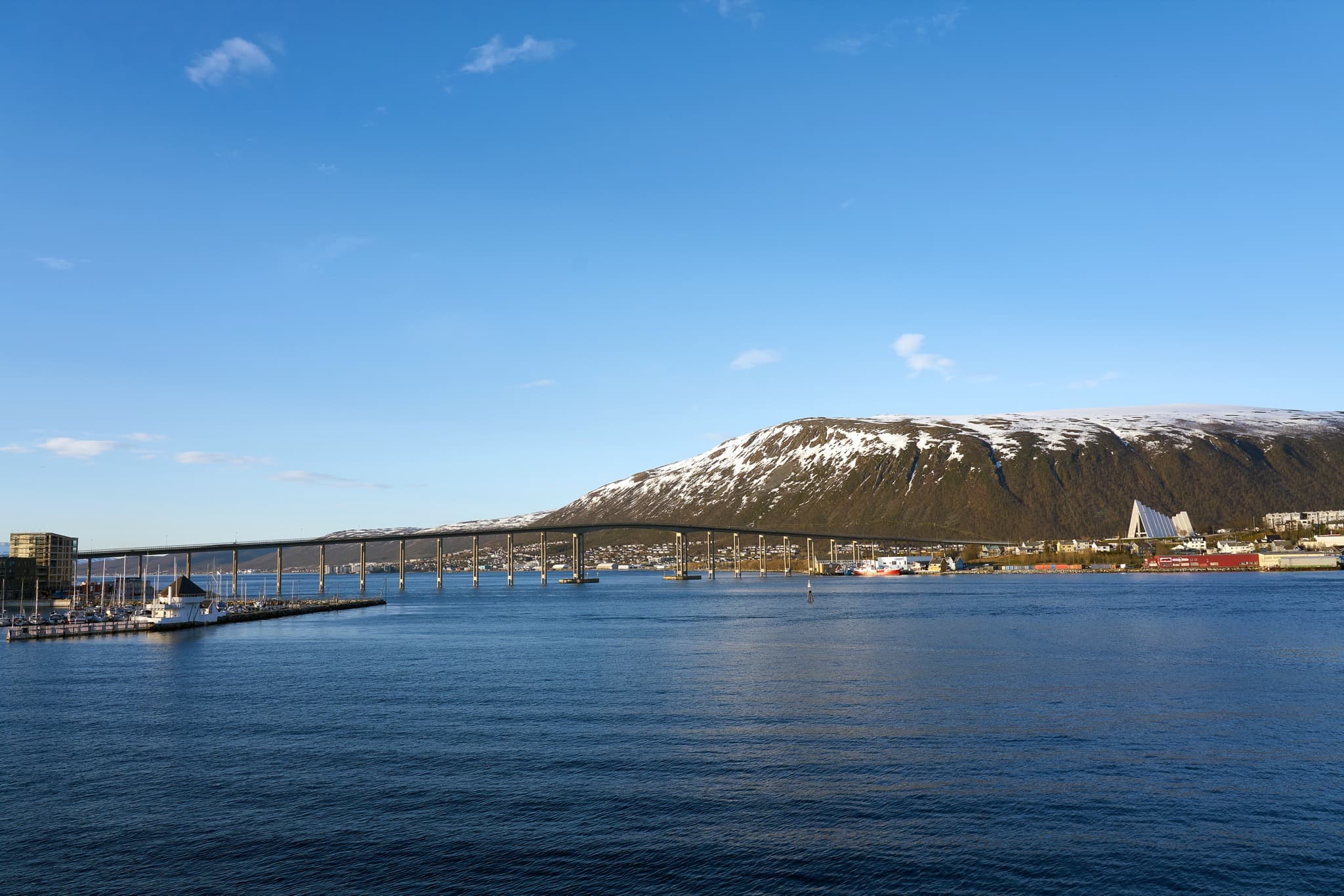 Illuminated triangular structure of the Arctic Cathedral reflecting across the water in Tromsø under the northern sky