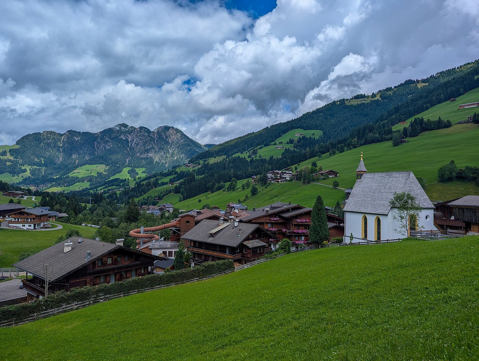 Traditional dark timber farmhouses with flower-draped wooden balconies nestled in the green Alpbachtal valley