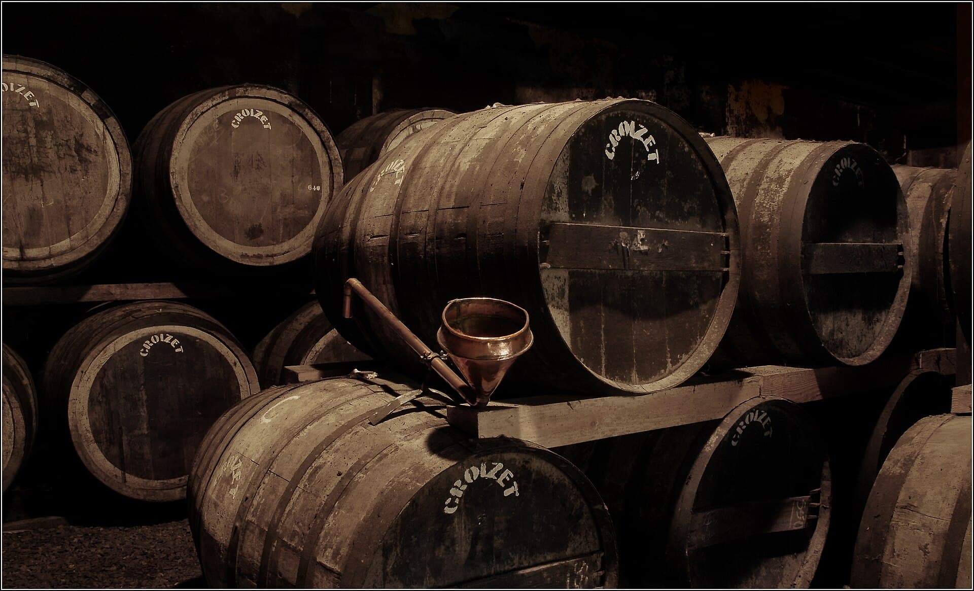 Amber glass of aged Cognac resting beside French oak barrels in a historic Charente cellar