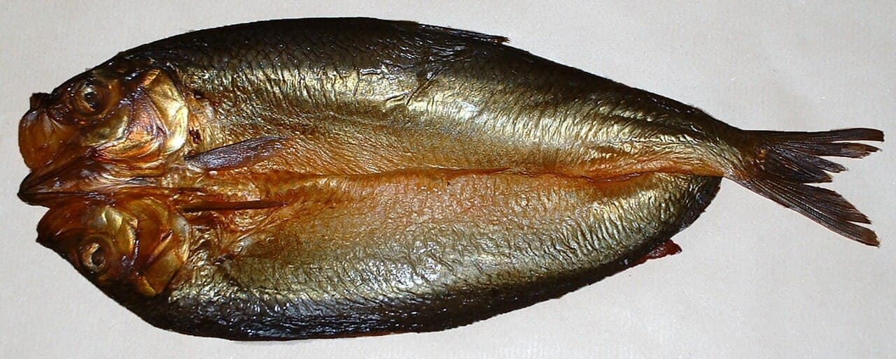 Golden oak-smoked whole kipper split open on a white serving plate