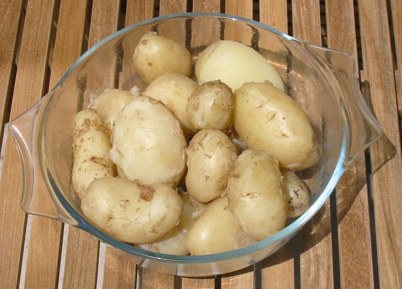 Steaming bowl of boiled Jersey Royal new potatoes tossed in fresh butter and herbs