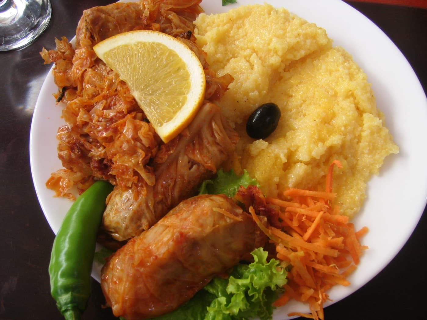 Clay baking dish of golden Romanian sarmale cabbage rolls served with polenta and peppers